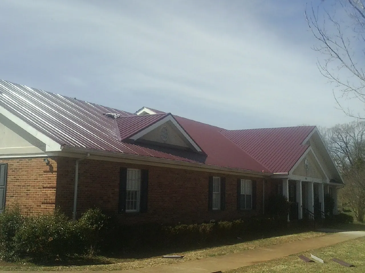Red metal roof with gabled entries on a long brick building, from a Hail Damage Roof Repair job in Maurice