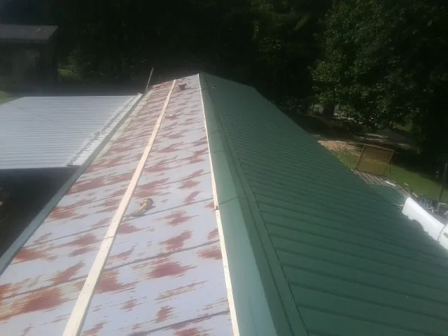 Old rusted panels beside newly installed green metal roofing — Wind Damage Roof Repair by Roofing Brothers in Maurice