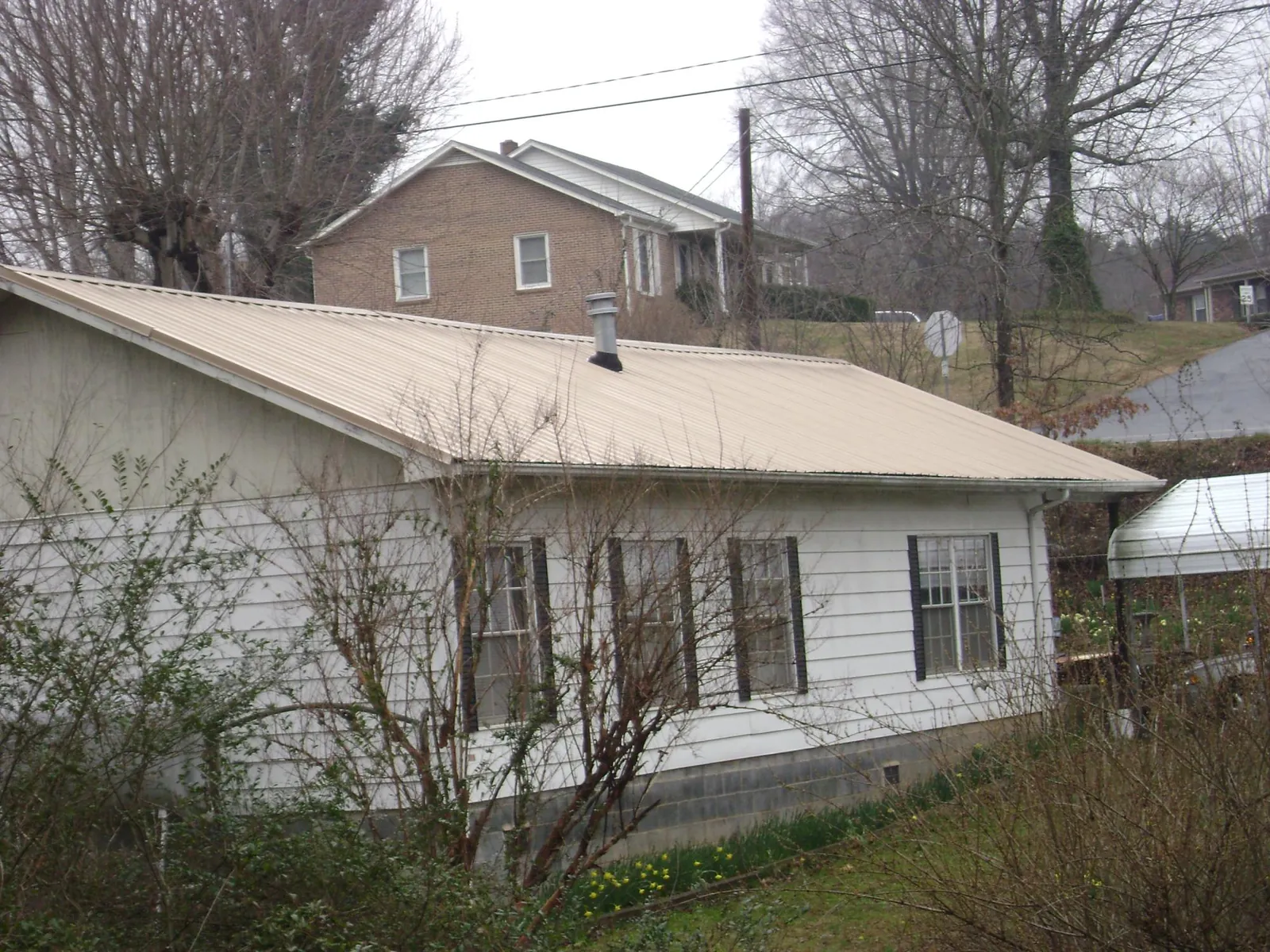 Tan metal roof on a white sided house set into a hillside — Commercial Roofing by Roofing Brothers in Maurice