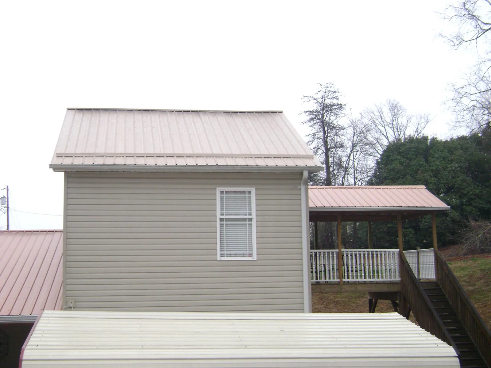 Tan metal roofs on a two story addition and attached porch, from a Roof Replacement job in Maurice